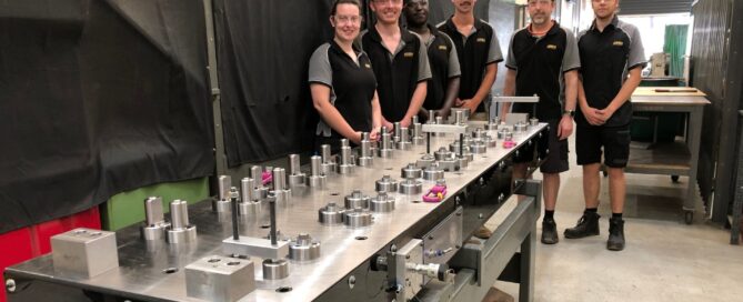 Five people from Axiom standing around a long table with space parts