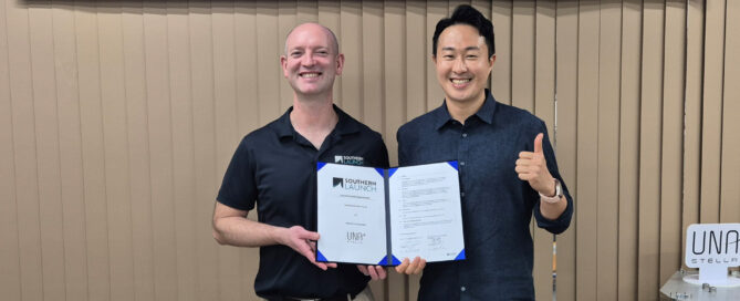 Two men at a launch facility holding a signed agreement