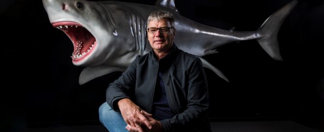 Photo of a man sitting in front of a model/design of a shark as part of a breakthrough announcement